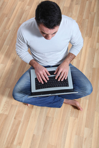 男子坐在地板上有便携式计算机上