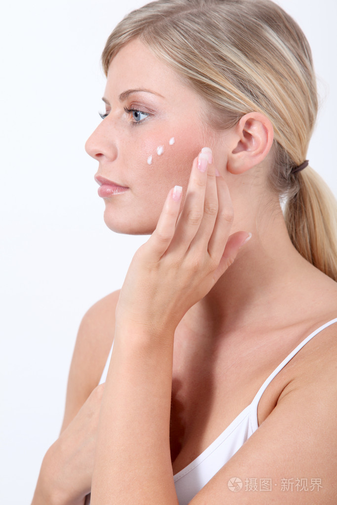 美丽的金发碧眼女人把面部保湿产品放在她的脸上