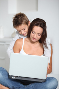 小男孩和母亲坐在沙发上在家里用的笔记本电脑