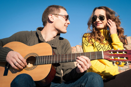 浪漫的年轻夫妇肖像在蓝蓝的天空下弹吉他