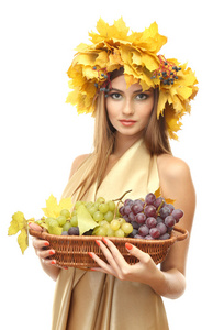 美丽的年轻女子，与黄色秋季花圈和葡萄在篮子里上白色, 隔离