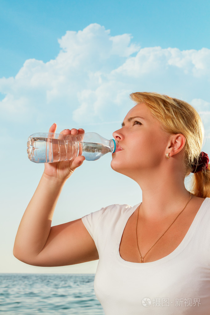 美丽的女人新鲜饮用水从瓶上热带东亚银行照片-正版商用图片1b7n5d-摄