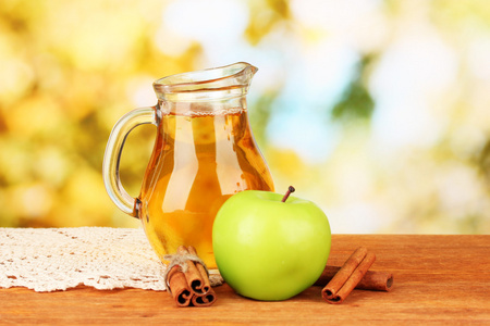 苹果汁和苹果在明亮的背景上的木桌上的充分 jug