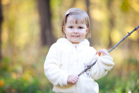 漂亮的小女孩用一根棍子上秋天的森林