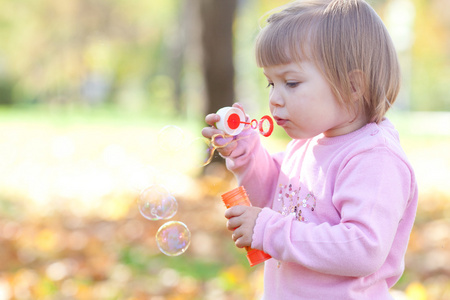 漂亮的小女孩制作泡沫鼓风机在秋天的森林