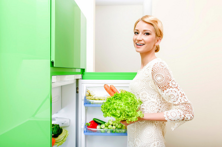 微笑着的年轻女子，进食蔬菜从冰箱