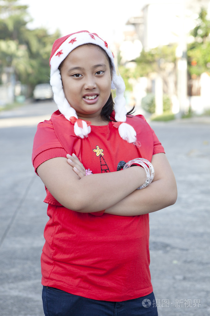 女孩在红色衬衫和圣诞老人的帽子站在村里的街道上