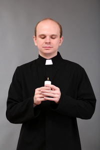 年轻牧师举行蜡烛在他的手，在灰色的背景上的肖像
