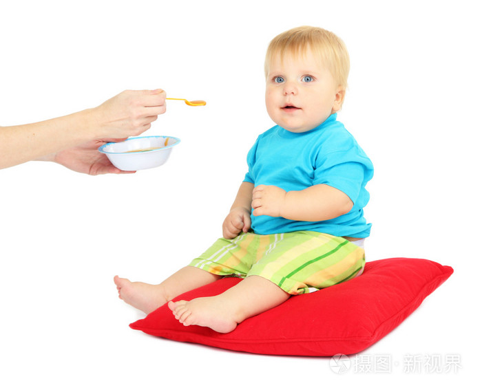 小男孩坐在红色的枕头上，吃苹果酱，孤立在白色