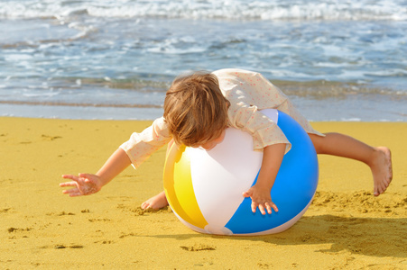 蹒跚学步女孩在海滩上玩她充气球