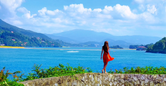 沿着石边境走的红裙子的女孩。在西班牙的美丽海景