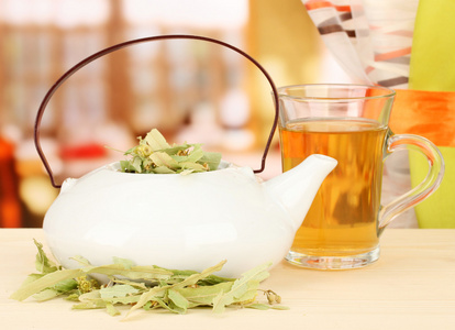 晒干的草药在木桌上，在明亮的背景上的茶壶。凉茶的概念照片