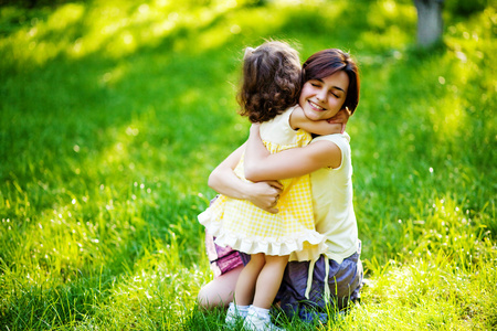 美丽的年轻母亲和她的女儿在绿色草地上很开心