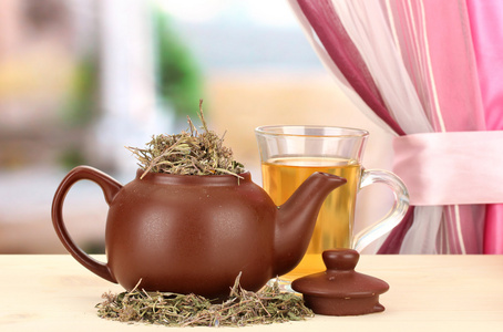 晒干的草药在木桌上，在明亮的背景上的茶壶。凉茶的概念照片