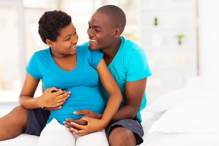 快乐的非洲裔美国孕妇和丈夫在床上拥抱