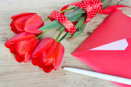 一束红色郁金香和木质信封背景。