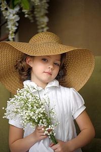 欧美女孩戴花小女孩笑着戴着宽边草帽,手里拿着一束山谷里的白色百合