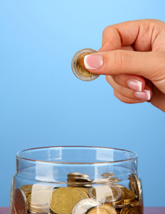 保存,将一枚硬币放入玻璃樽,在彩色背景上的女性手照片