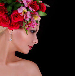 时装模特与发型与美丽的花朵在黑色背景 红玫瑰 粉红鸢尾花在她的头发的年轻女人