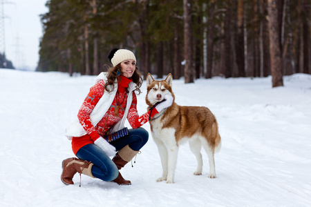 快乐的女人玩冬季森林的西伯利亚爱斯基摩狗照片
