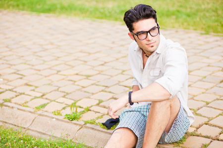英俊的男人戴着眼镜坐在人行道上寻找阿波