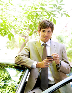 有吸引力的年轻商人，靠在他的车的门上的同时使用数字平板电脑