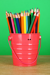 在桶上绿色背景表格中的彩色铅笔
