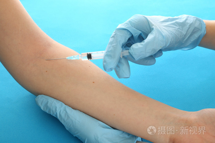 医生控股注射器与一种疫苗在病人手,蓝色背景上