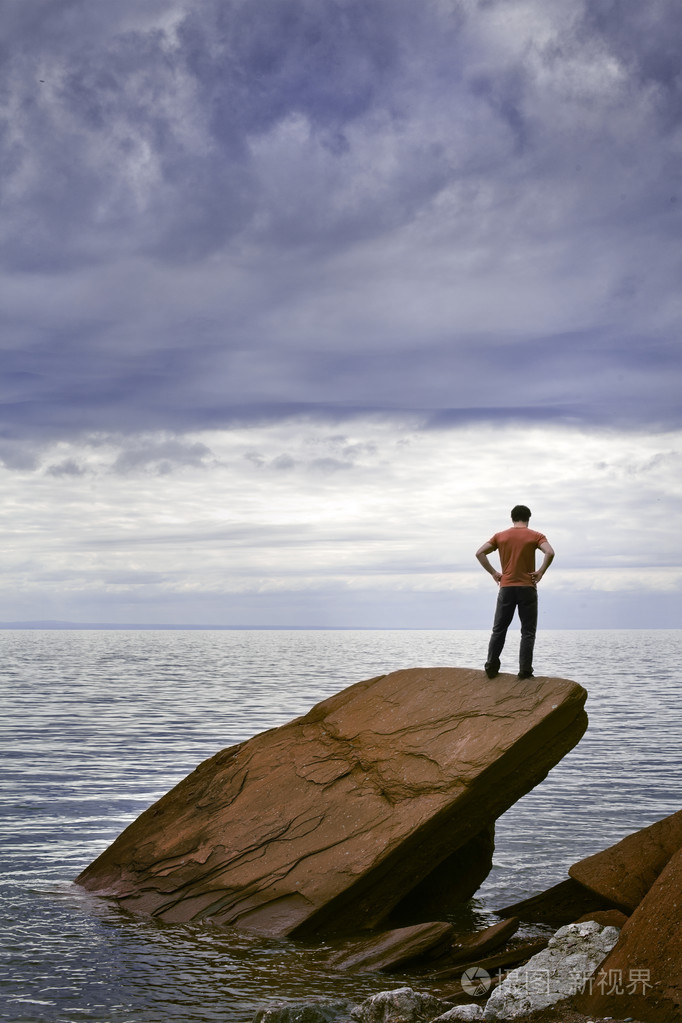 一个年轻的男人站在海边岩石上