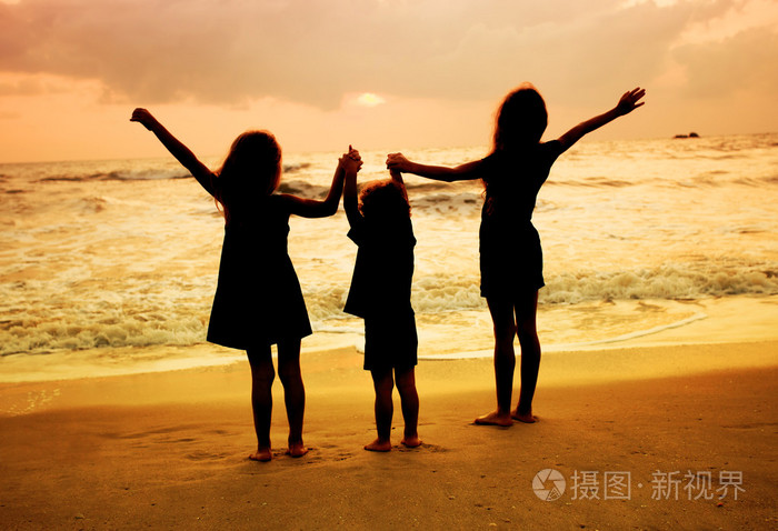 三个孩子站在海滩上在日落时的剪影