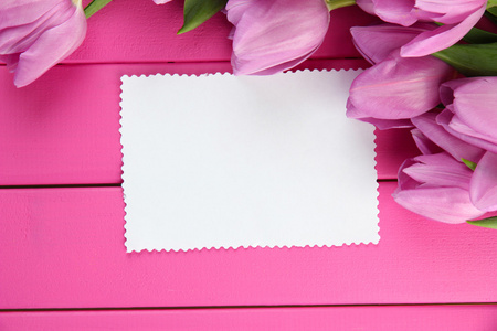 束美丽的紫色郁金香和粉红色的木制背景上的空白卡