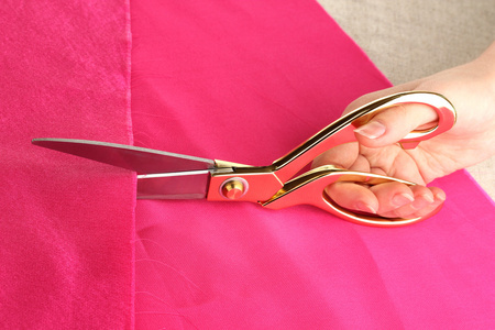 女裁缝师剪粉色面料米色织物背景上