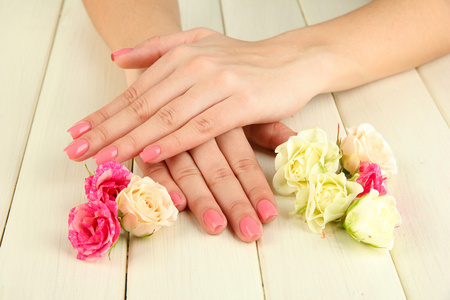 女人手中粉红色修指甲和鲜花的木制背景