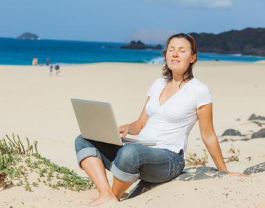 女子坐在海滩上的笔记本电脑