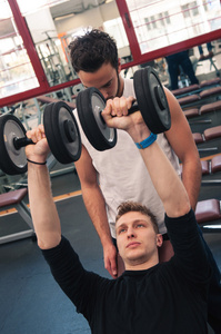 年轻的男人和他的哑铃在健身房锻炼的个人教练