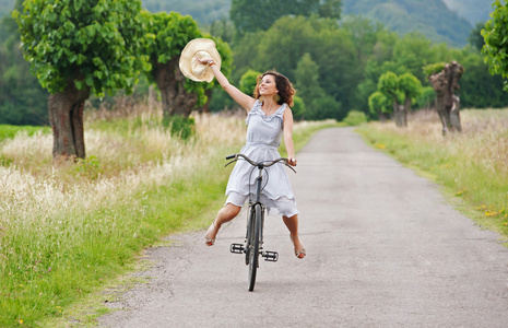漂亮的年轻女人骑自行车在乡村小路上