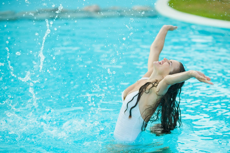 快乐的年轻女人泼在游泳池中的水