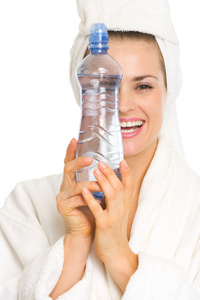 微笑的年轻女士穿着浴衣躲在水的瓶子