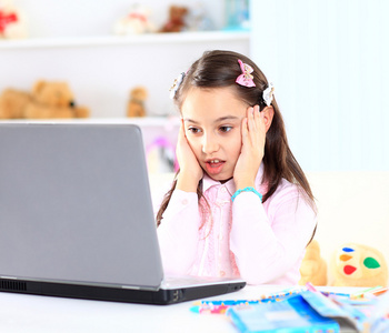 可爱的小女孩微笑着和看着笔记本电脑，使用的便携式计算机的小女孩