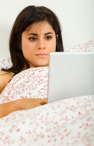 年轻漂亮的女人躺在床上的笔记本电脑与工作