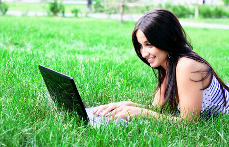 迷人的黑发女人在夏天草地上的一台笔记本电脑