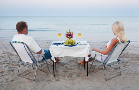 一对年轻夫妇与蜡烛和酒杯海砂海滩上的共享浪漫的晚餐