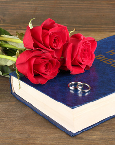 圣经上与玫瑰木制背景上的结婚戒指