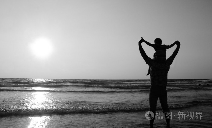 父亲和儿子在日落时在海边散步黑色和白色p