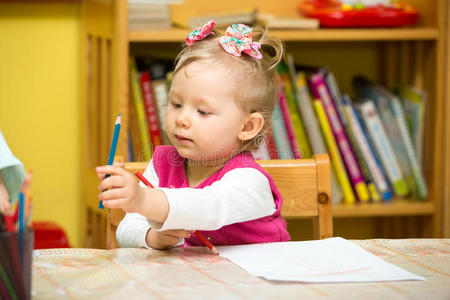 可爱的小女孩在幼儿园桌边用彩色铅笔画画