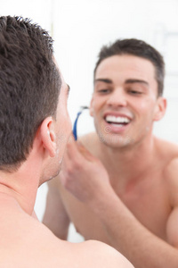 微笑的男人在浴室里刮胡子，为一天做准备