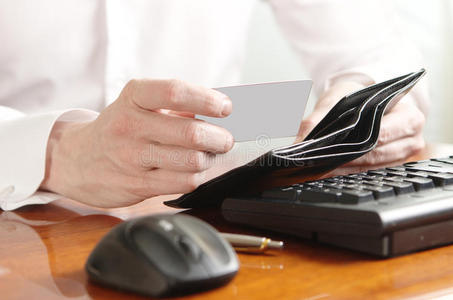 电脑键盘上放着钱包和银行卡的商人的手