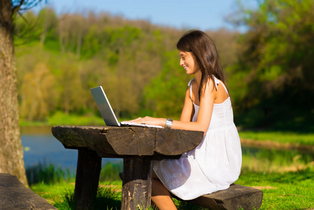 年轻女性用一台笔记本电脑，坐在一个美丽的湖