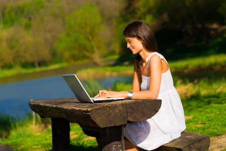 年轻女性用一台笔记本电脑，坐在一个美丽的湖