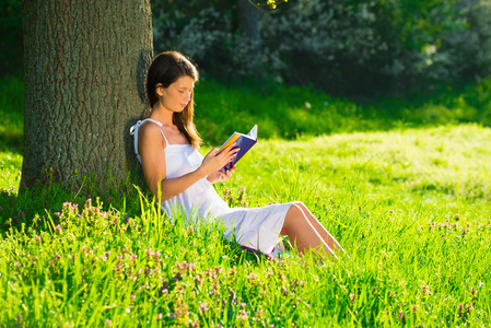 一个年轻女子躺在草地上，和读一本书